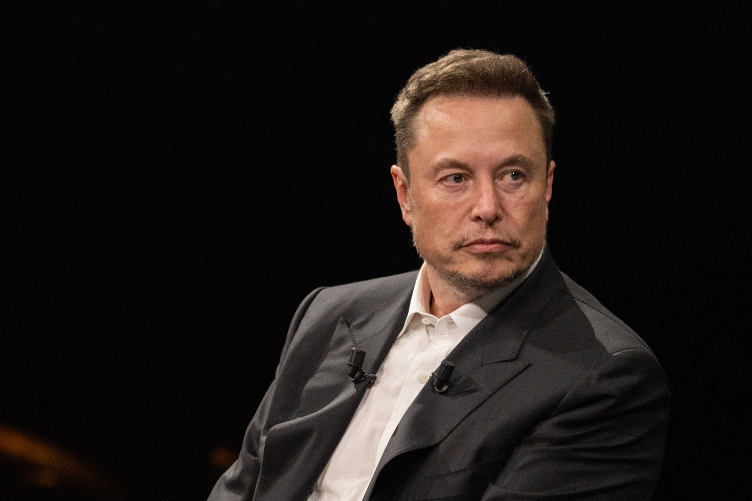 Elon musk sitting in chair looking pensive